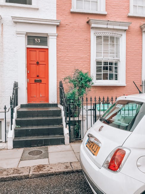 Exterior view of a pink and white terraced house with the number 53 displayed above a vibrant red front door, accessed by a short staircase with black iron railings. A small green shrub is situated ne