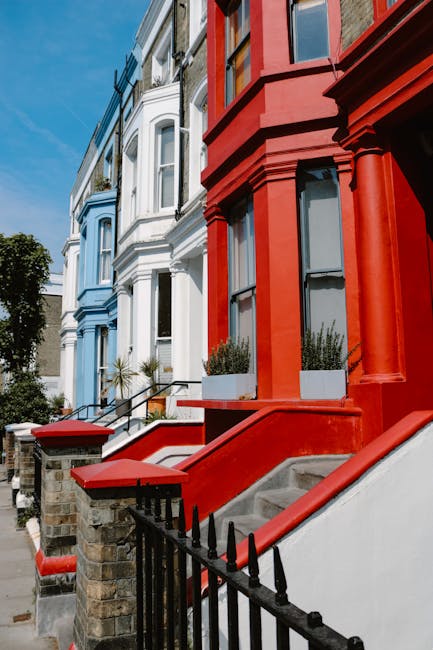 The image depicts a busy street scene in Notting Hill with a crowd of pedestrians walking along the pavement and crossing the road. On the left side, a row of parked cars lines the street, with some b